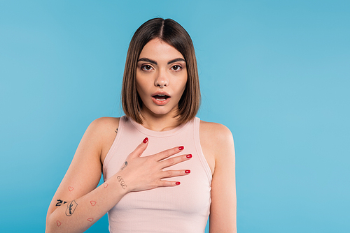 shocked woman with hand on chest, stylish model with tattoos and nose piercing looking at camera on blue background, emotional, opened mouth, generation z, summer fashion