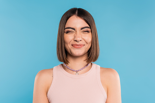 positivity, cheerful young woman with short hair, nose piercing and tank top smiling on blue background, generation z, fashionable, personal style, silver necklace, emotional, happiness