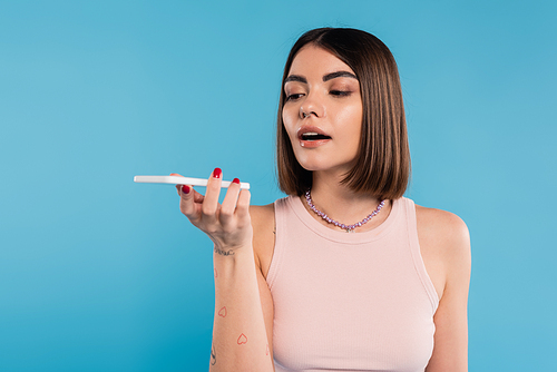 voice message, young woman with short hair, tattoos and nose piercing using smartphone on blue background, casual attire, gen z fashion, personal style, social media influencers