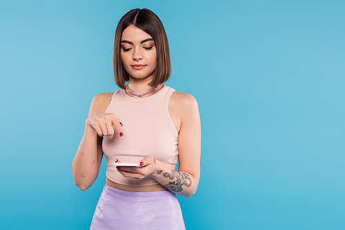 sending a message, young brunette woman short hair, tattoos and nose piercing using mobile phone on blue background, casual attire, gen z fashion, social media influencers
