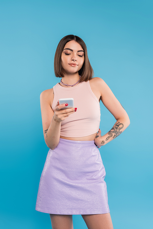 sending a message, attractive young woman short hair, tattoos and nose piercing using mobile phone on blue background, casual attire, gen z fashion, social media influencers