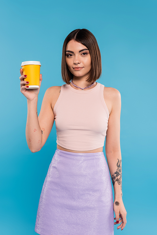 coffee to go, attractive young woman with short hair, tattoos and nose piercing holding paper cup on blue background, generation z, summer trends, hipster style