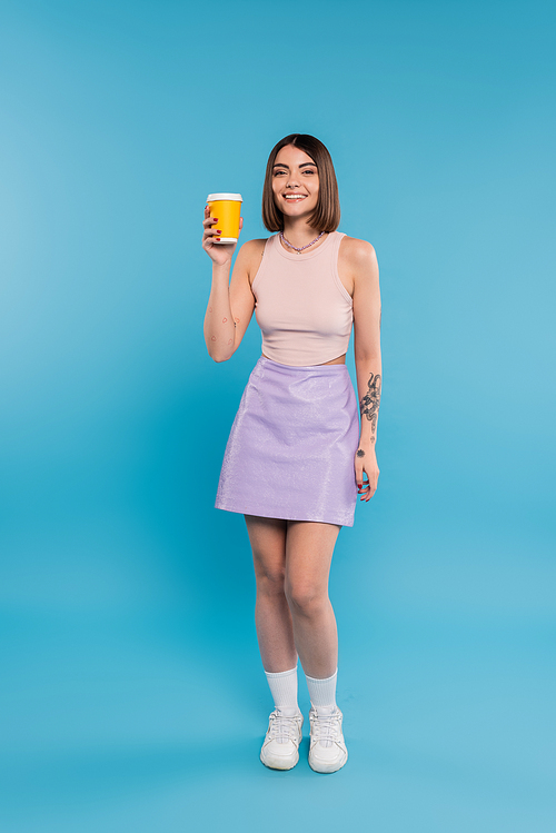 coffee to go, cheerful young woman with short hair, tattoos and nose piercing holding paper cup on blue background, generation z, summer trends, attractive, coffee culture