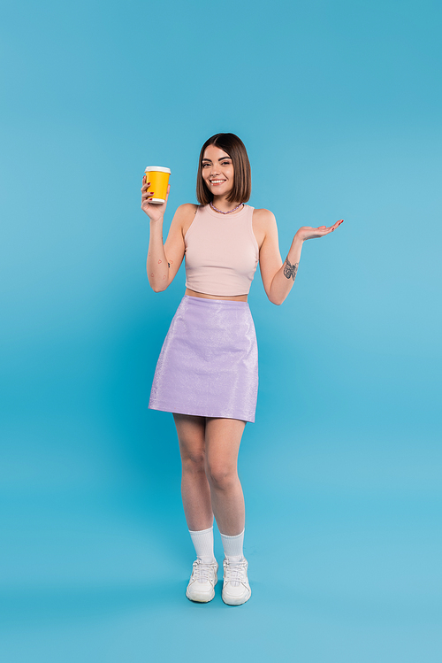 coffee to go, happy young woman with short hair, tattoos and nose piercing holding paper cup on blue background, generation z, summer trends, attractive, coffee culture, everyday style