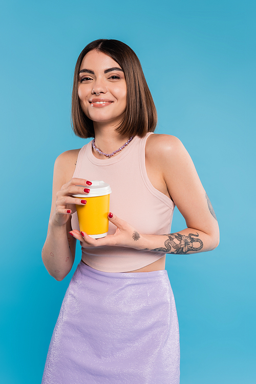 to go coffee, happy young woman with short hair, tattoos and nose piercing holding paper cup on blue background, generation z, summer trends, attractive, coffee culture, everyday style