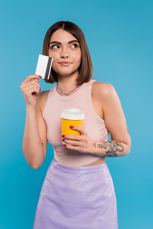 to go coffee, young woman with short hair, tattoos and nose piercing holding paper cup and credit card on blue background, generation z, summer trends, attractive, coffee culture, dream