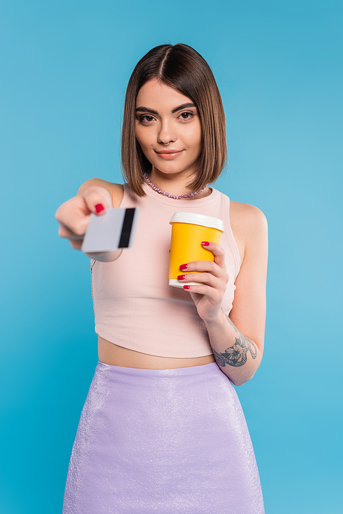 to go coffee, happy young woman with short hair, tattoos and nose piercing holding paper cup and giving credit card on blue background, generation z, summer trends, attractive, coffee culture