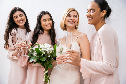 positivity, blonde bride in wedding dress holding bouquet, standing with interracial bridesmaids, champagne glasses, grey background, racial diversity, fashion, multicultural young women