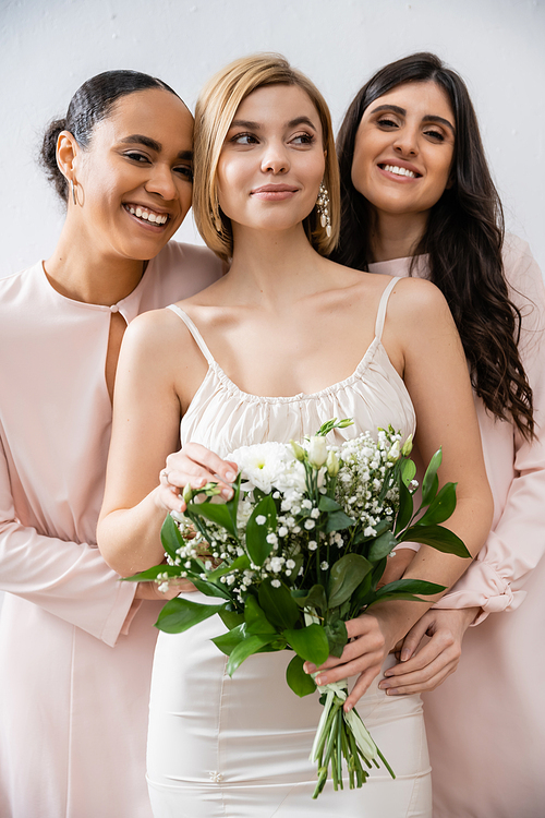 special occasion, brunette and interracial bridesmaids hugging blonde bride, friendship goals, grey background, happy multicultural girlfriends, cultural diversity, bridal bouquet, bridal party