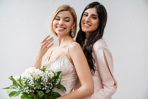 special occasion, bridesmaid hugging bride, showing engagement ring, friendship goals, grey background, happy girlfriends, bridal bouquet, blonde and brunette women, white flowers, happiness