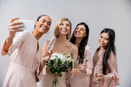 four women, cheerful bride and her multicultural bridesmaids taking selfie together, happiness, champagne glasses, bridal bouquet, wedding dress, brunette and blonde women