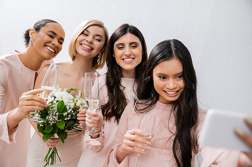 four women, positive blonde bride and her interracial bridesmaids taking selfie together, champagne glasses, bridal bouquet, wedding dress, bridesmaid gown, brunette and blonde women