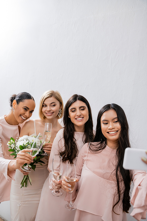 four women, cheerful blonde bride and her interracial bridesmaids taking selfie together, happiness, champagne glasses, bridal bouquet, wedding dress, bridesmaid gown, brunette and blonde women