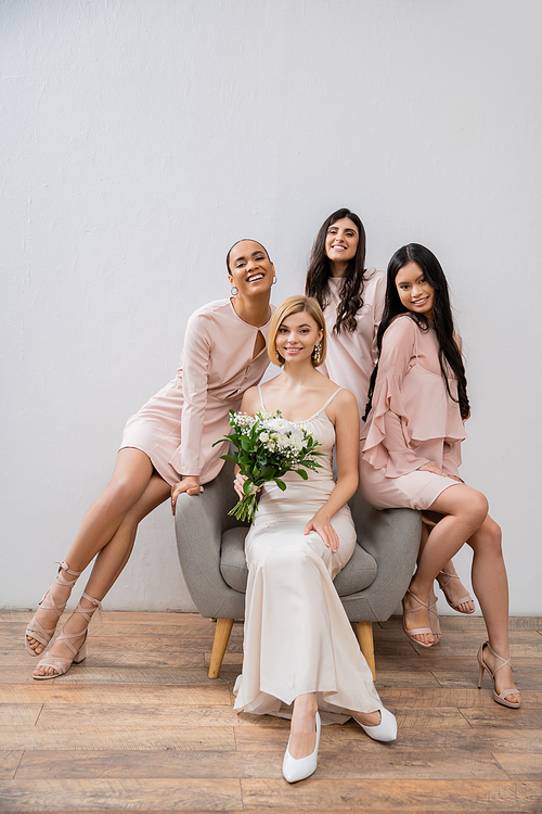 wedding photography, happy four women, bride and bridesmaids, interracial girlfriends, wedding day, cultural diversity, sitting on armchair, grey background, happiness and joy, bridal gown