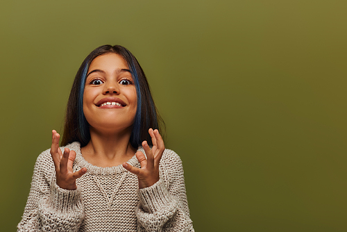 Thrilled preteen girl with dyed hair wearing trendy knitted sweater while gesturing and looking at camera while standing isolated on green, stylish girl in cozy fall attire concept