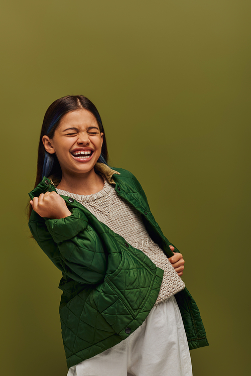 Excited and stylish preadolescent girl with dyed hair showing yes gesture while posing in autumn jacket and knitted sweater isolated on green, modern fall fashion for preteens concept