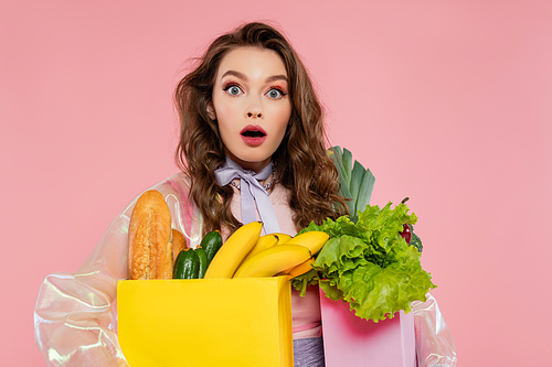 housewife concept, shocked young woman carrying grocery bags with vegetables and bananas, model with wavy hair on pink background, conceptual photography, home duties, stylish wife