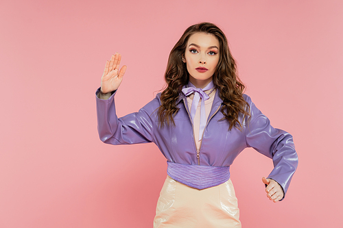 glamour, attractive young woman with wavy hair gesturing and looking at camera, pretending to be a doll, trendy outfit, model in purple jacket posing on pink background, studio shot, conceptual