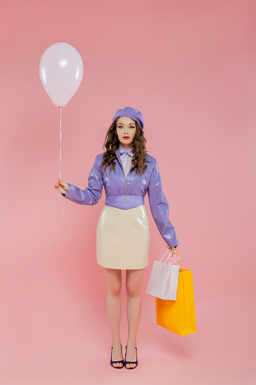 fashion photography, attractive and young woman holding balloon and shopping bags on pink background, posing like a doll, standing and looking at camera, trendy, consumerism, purple outfit
