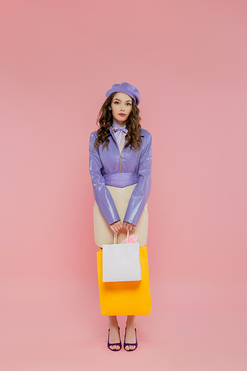 consumerism, fashion photography, attractive young woman in beret holding shopping bags on pink background, posing like a doll, standing and looking at camera, trendy outfit, consumerism
