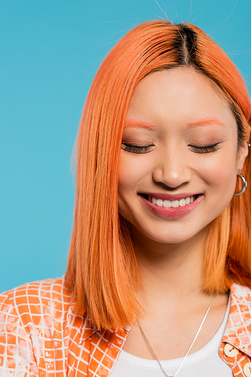 portrait, cheerful face, young asian woman with short and dyed hair, natural makeup and hoop earrings smiling on blue background, orange shirt, generation z, happiness, emotion of joy