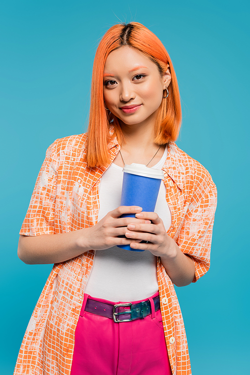 drink in hands, happy asian and young woman with red hair holding paper cup and looking at camera on blue background, casual attire, generation z, coffee culture, hot beverage, single use cup