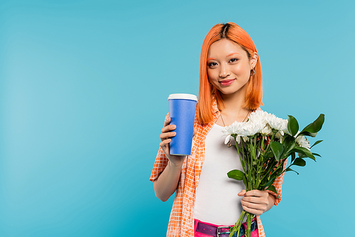positivity, happy asian and young woman with red hair holding coffee to go in paper cup and bouquet of flowers on blue background, casual attire, generation z, coffee culture, hot beverage