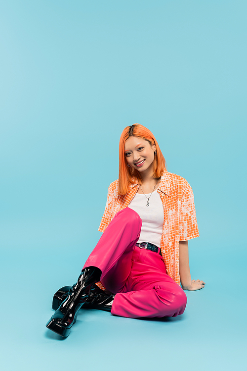 happy summer, young asian woman with radiant smile and dyed red hair looking at camera on blue background, trendy casual attire, pink pants, orange shirt, generation z lifestyle