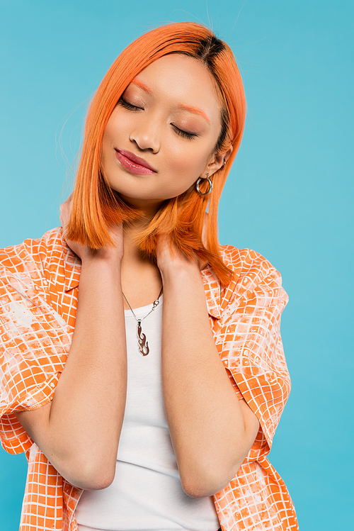 summertime happiness, radiant smile, young and charming asian woman with colored red hair posing with closed eyes and in orange shirt on blue background, generation z