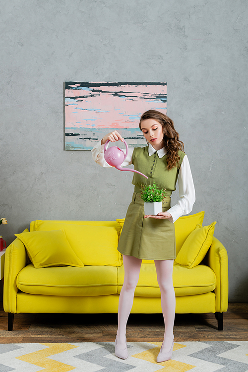 eco-friendly, housekeeping concept, young woman with brunette wavy hair watering plant, green thumb, botany, indoor gardening, housekeeping, beautiful housewife standing in living room