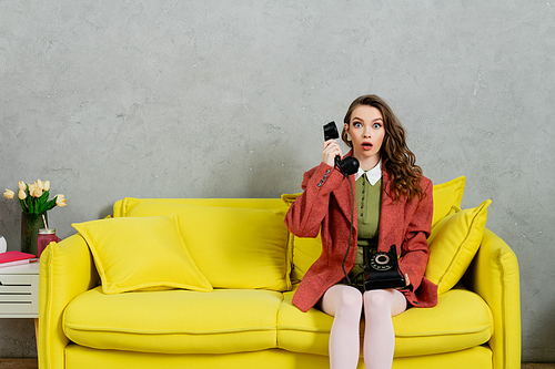 phone call, attractive woman with wavy hair sitting on yellow couch, housewife talking on retro telephone, acting like a doll, looking at camera with opened mouth, shock, grey wall