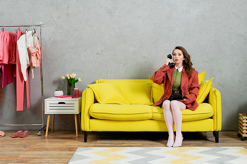 phone call, attractive woman with wavy hair sitting on yellow couch, housewife talking on retro telephone, posing like a doll, looking away, modern interior, living room