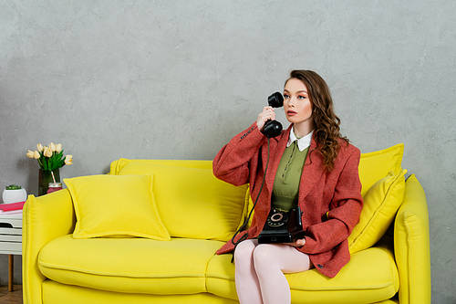 vintage vibes, attractive woman with wavy hair sitting on yellow couch, housewife talking on retro telephone, posing like a doll, looking away, modern interior, living room