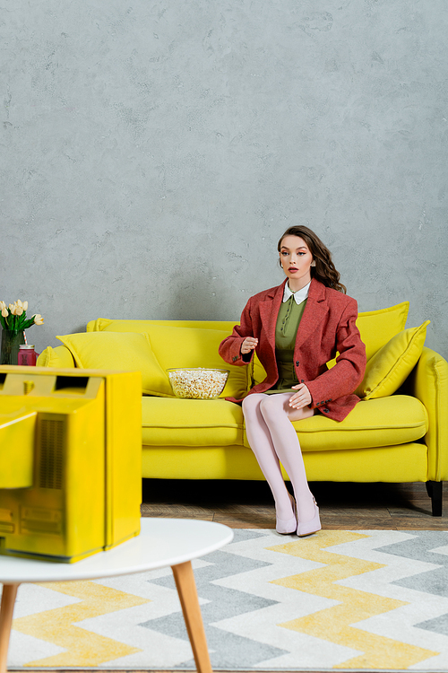 woman acting like a doll, concept photography, model with brunette wavy hair sitting on yellow couch next to bowl of popcorn, watching tv, home entertainment, leisure, concept photography