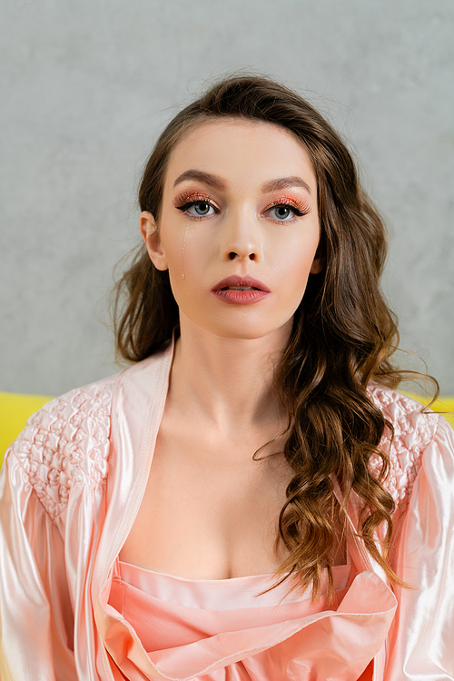 portrait of beautiful young woman with brunette wavy hair looking at camera, headshot, pink robe, housewife with evening makeup, doll concept, feminine youth