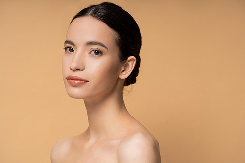 Young asian woman with naked shoulders and natural makeup looking at camera isolated on beige