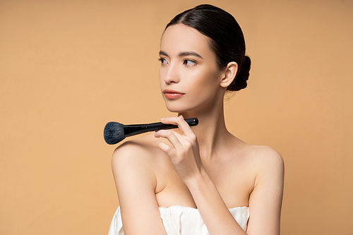 Young asian woman in top holding blush brush near naked shoulders isolated on beige