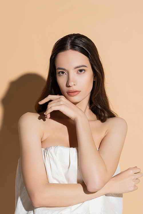 Pretty young asian woman in top looking at camera and posing on beige background