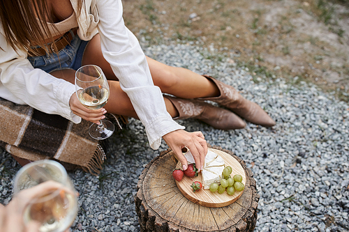 High angle view of young woman holding wine and taking fruits near cheese and boyfriend outdoors