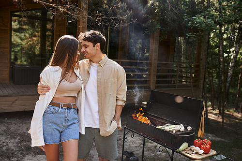 happy man hugging  girlfriend near barbecue grill, summer romance, couple, vacation house