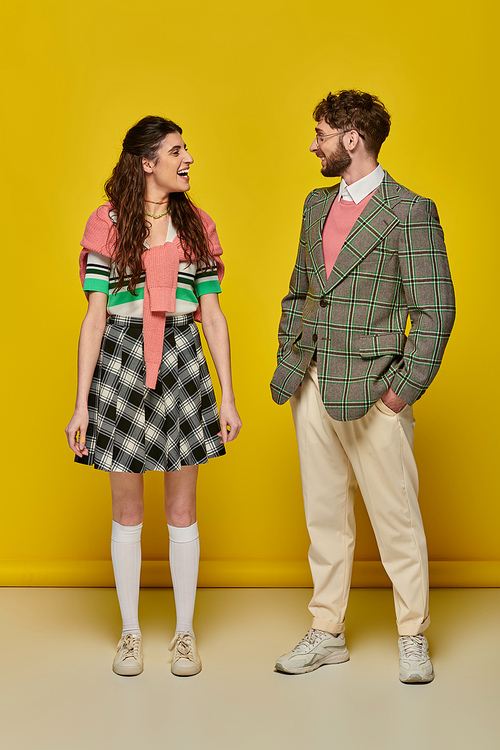 positive students looking at each other on yellow backdrop, happy man and woman in college outfits