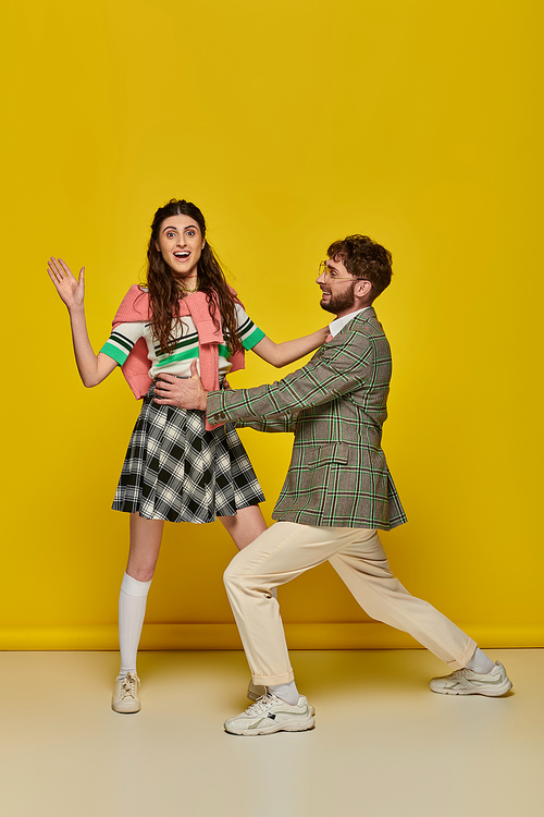 young couple having fun, man in glasses hugging young woman on yellow backdrop, students, outfits