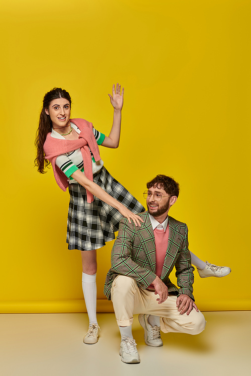 funny couple, happy young man and woman gesturing, posing on yellow backdrop, student outfits