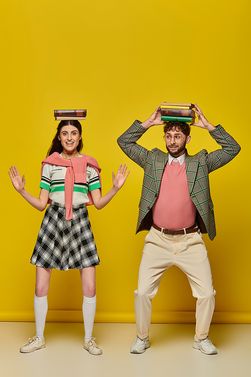 funny couple, happy young man and woman standing with books on heads on yellow backdrop, students