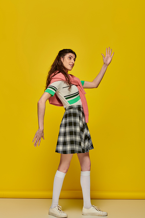 young woman acting like a doll, gesturing unnaturally, standing on yellow backdrop, student