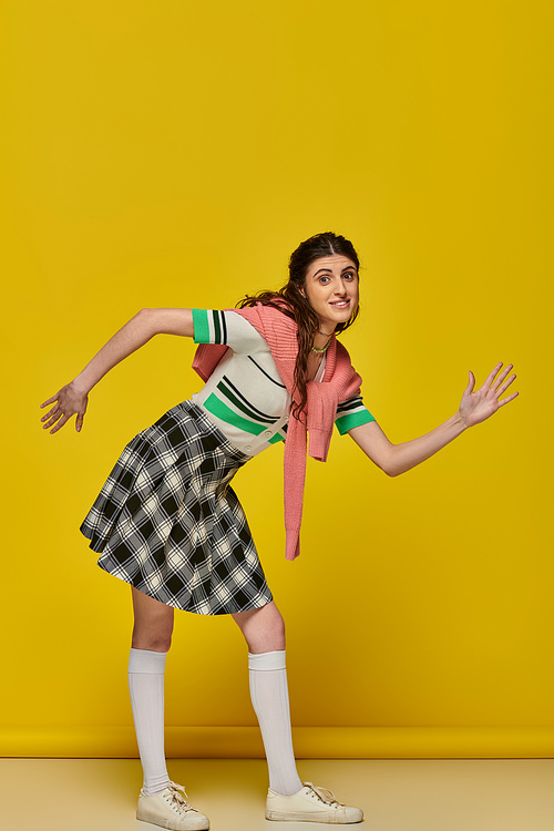happy woman acting like a doll, gesturing unnaturally, standing on yellow backdrop, young student