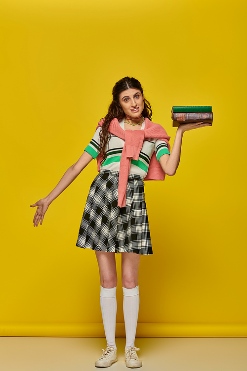 young student with books, brunette woman in checkered skirt posing on yellow backdrop, brunette