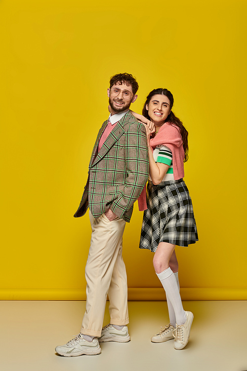 happy students, young woman leaning on man in glasses, college outfits, yellow backdrop, couple