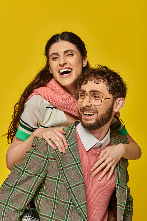 funny students, cheerful man piggybacking young woman on yellow backdrop, college outfits, couple