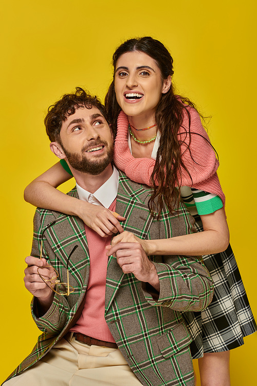 excited woman hugging bearded man, holding glasses, yellow backdrop, college outfits, students